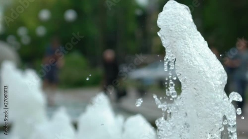 closeup of fontain jet in the park with defocused people on background. Slow motion