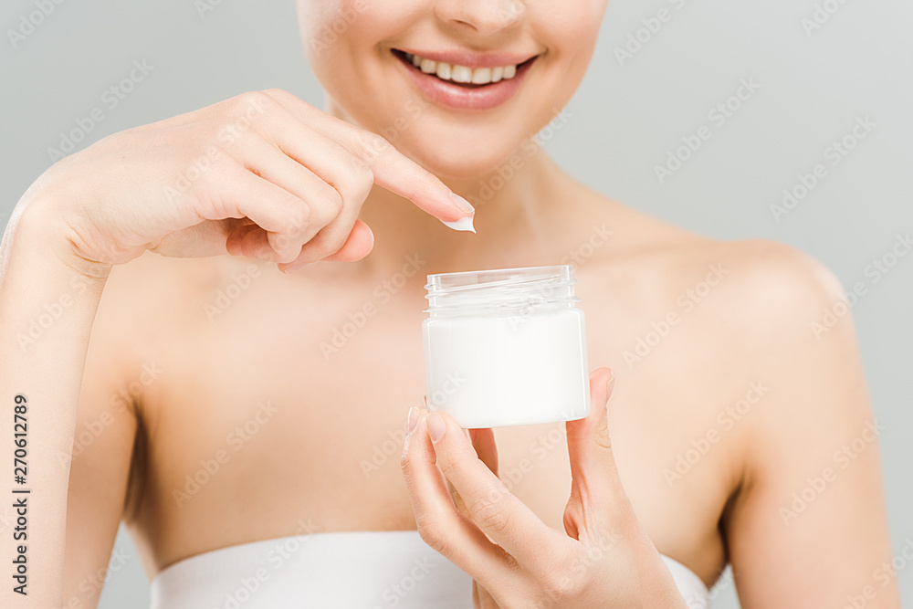 cropped view of smiling woman holding container with face cream isolated on grey cropped view of smiling woman holding container with face cream isolated on grey