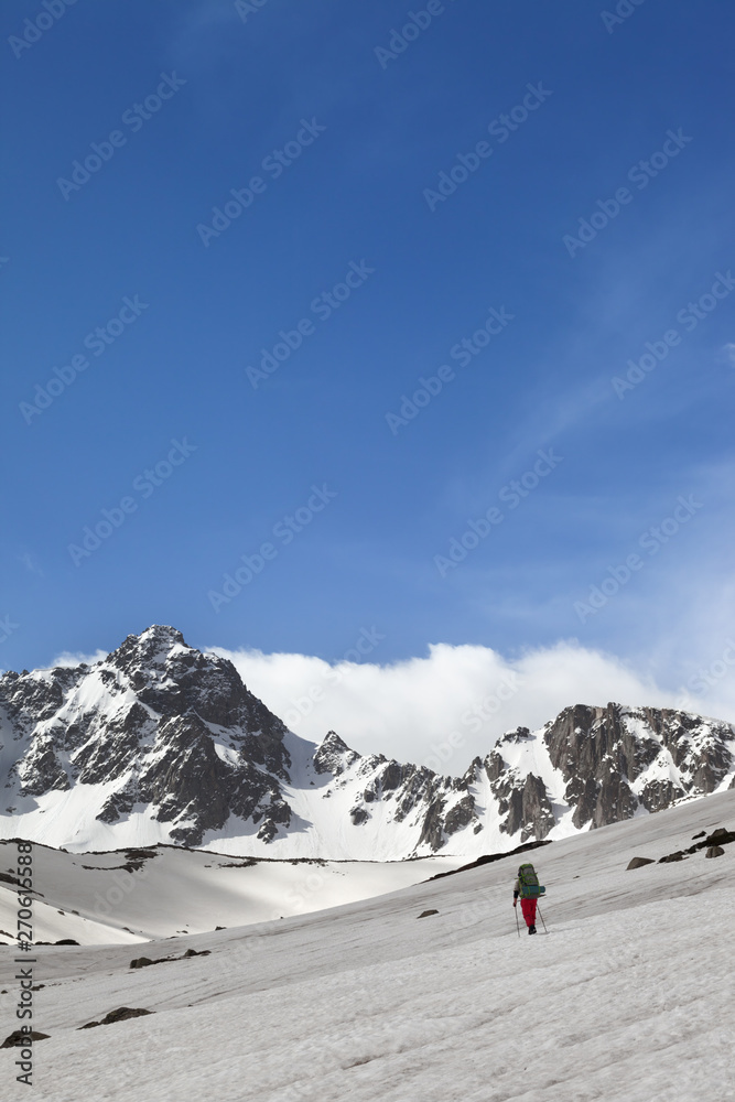 Hiker on snowy plateau, snow covered mountain range and sunlit sky