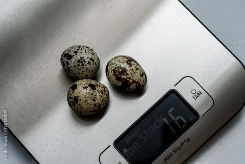 Quail eggs are on the table scales. The scoreboard shows the weight of eggs in grams. The background of the image is white. Selective focus. Copy space. photo