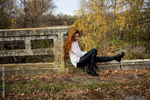 Portrait of young redhead woman sitting on a bench in autumn park photo