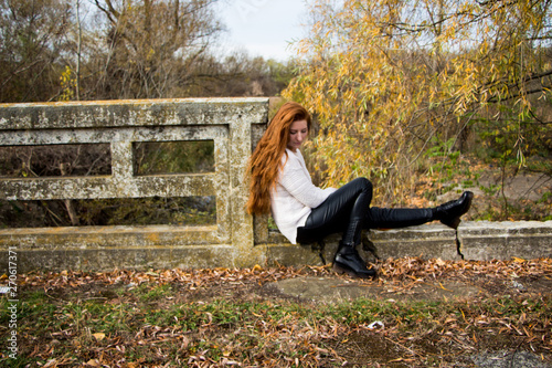 Portrait of young redhead woman sitting on a bench in autumn park photo