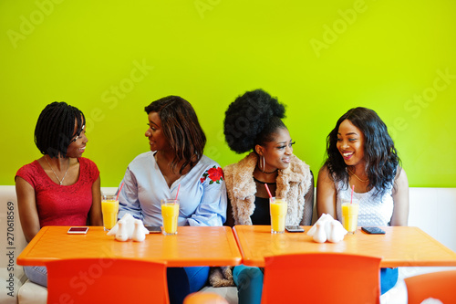 Four young african girls with juices sitting in bright colored fast food restaurant.