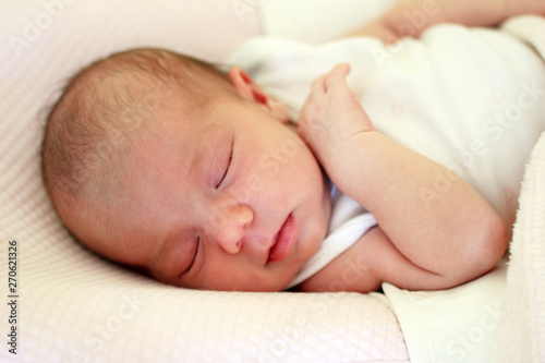 Portrait of cute newborn baby sleeping on a pink bed under beige blanket.