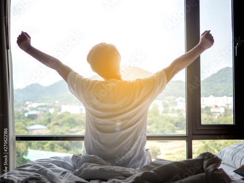 Man stretch his hands after waking up in bed at morning with sunlight