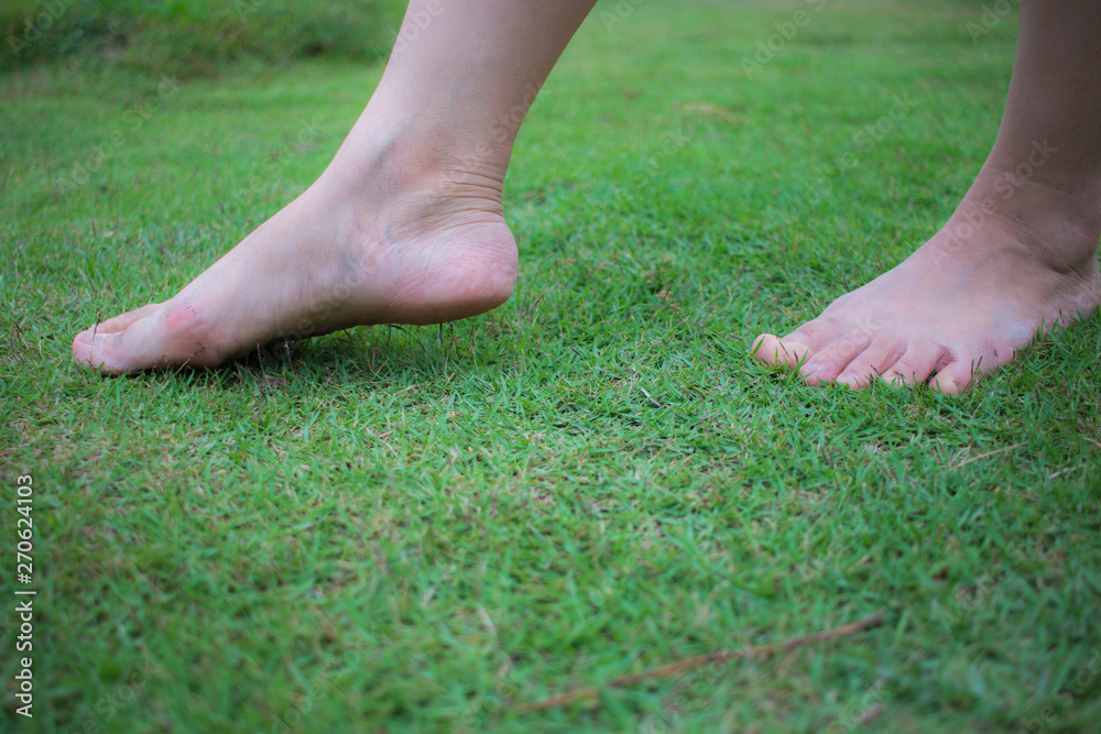 Young woman's barefoot walking on the fresh, green grass in sunny summer in the morning. Restful moment. Healthy lifestyle. Bright color. Close up. Back view. Go away.