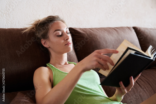 Attractive blonde woman in green top reading book on sofa.