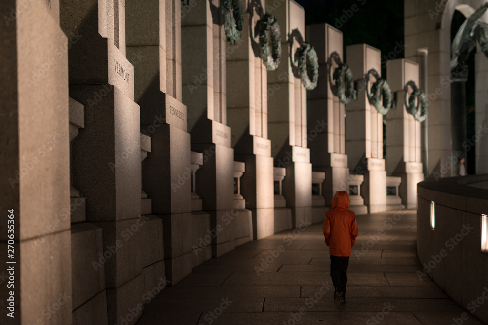 Boy alone at night walks quietly reflecting through World War II memorial Boy alone at night walks quietly reflecting through World War II memorial