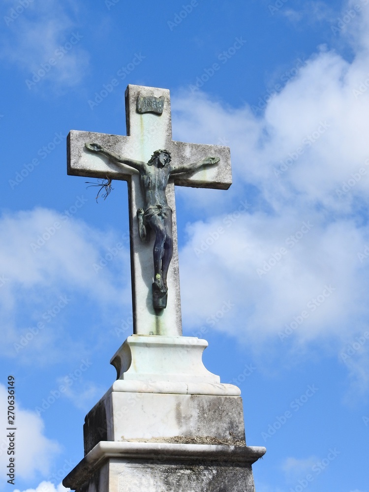 Scene in a cemetery: close-up of a large stone crucifix illuminated by the sun. Blue sky with some clouds on a sunny day.