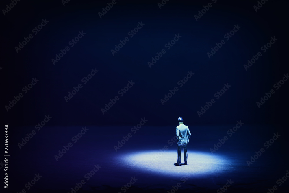 A picture of a miniature man stands in the spotlight looking forward.Concept of facing the unknown, taking a decision and finding solution. - obrazy, fototapety, plakaty 