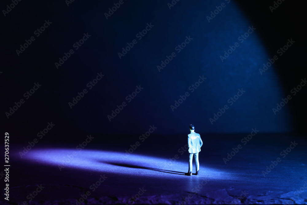 A picture of a miniature man stands in the spotlight looking forward.Concept of facing the unknown, taking a decision and finding solution.