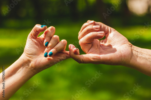 Closeup shot of hands making a pinkie promise sign in nature – Mother and daughter crossing their little fingers in symbol of commitment photo