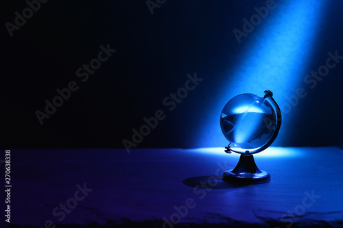 Small crystal globe in front of dark and dramatic light.global issues concept