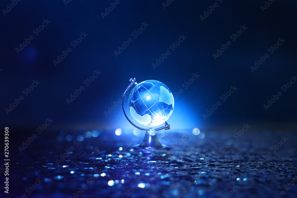 Small crystal globe in front of dark and dramatic light.global issues concept - obrazy, fototapety, plakaty 