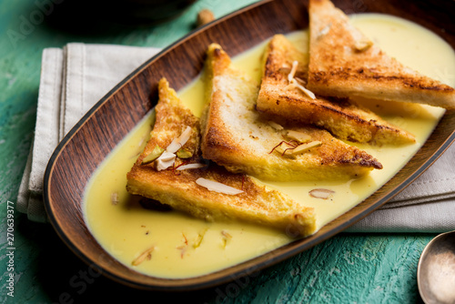 shahi tukra/tukda or Double ka meetha is a bread pudding Indian sweet of fried bread slices soaked in rabid or sweet saffron milk garnished with dry fruits, selective focus photo