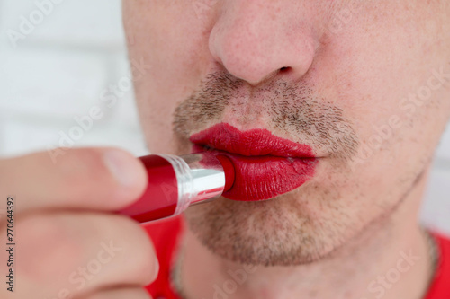 Portrait, man with a bristle applying colorful red lip lipstick on his lips, side view, close up