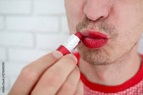 Portrait, man with a bristle applying colorful red lip lipstick on his lips, side view, close up