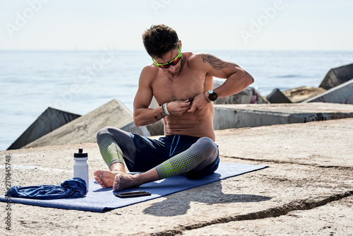 Sportsman in pulsometer sitting on mat on seafront photo