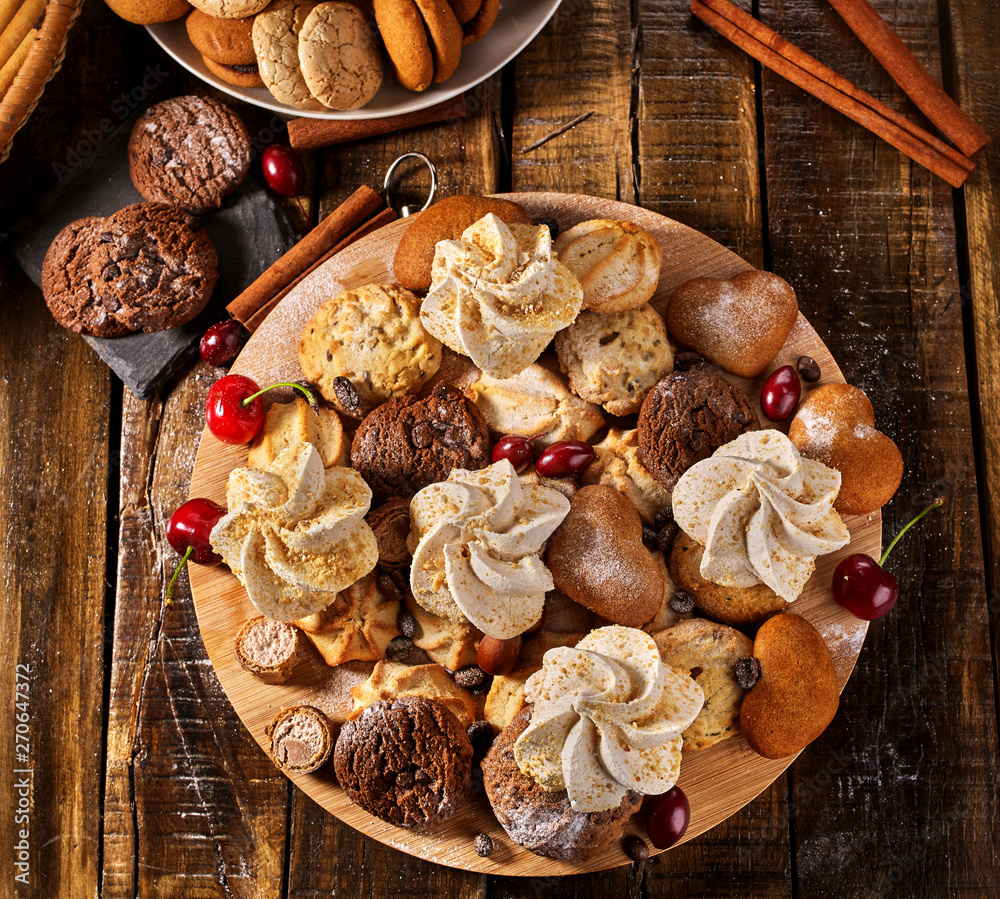 Fototapeta premium Oatmeal cookies and sand chocolate cake with cherry berry and crispy wafer rolls with cream on cutting board on wooden table in rustic style. Limitations for diabetics. Yummy.