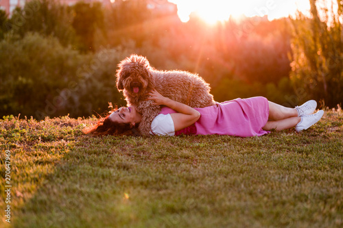 young owner woman with her brown spanish water dog having fun outdoors in a park at sunset. love for animals concept photo