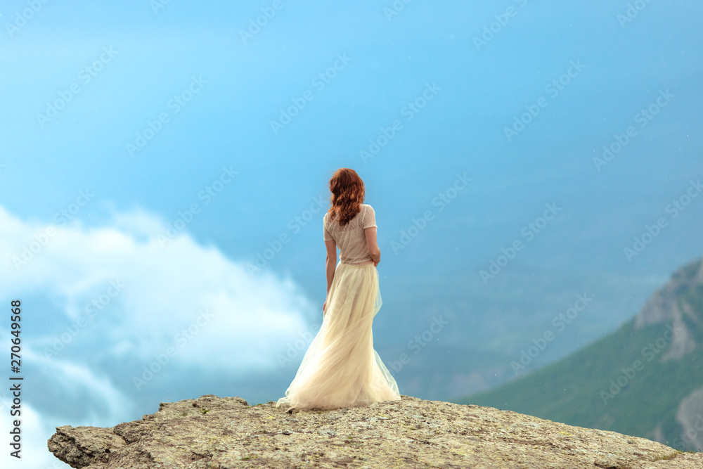 A girl in a dress and hat admiring the dawn or sunset of the sun in a picturesque place in the mountains. A girl in a dress and hat admiring the dawn or sunset of the sun in a picturesque place in the mountains.