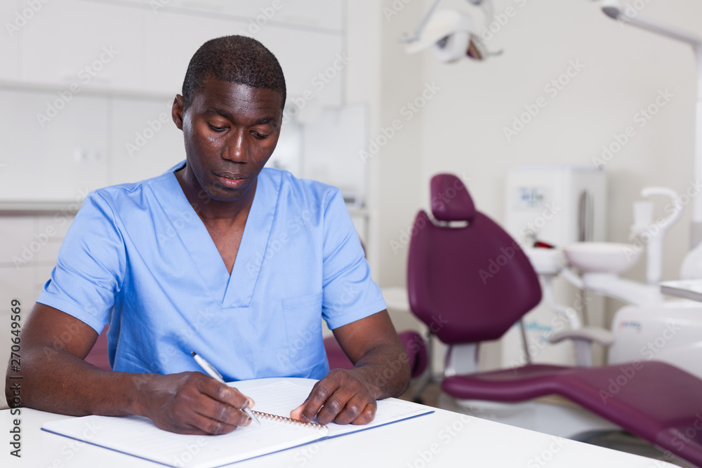 Fototapeta premium Confident male dentist working with medical records in dental office