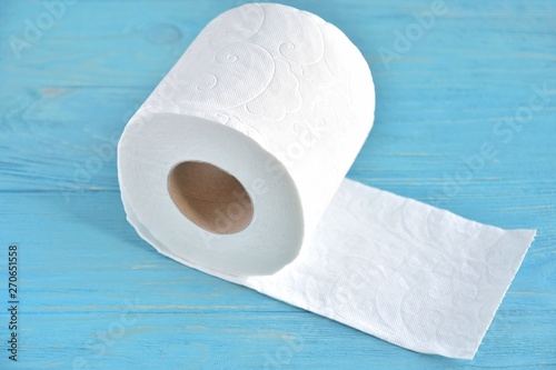 A roll of soft white toilet paper with selective focus on textured wooden background. Restroom concept with toilet paper on blue wood backdrop. Daily hygiene cleanser. Recycling toilet paper. 