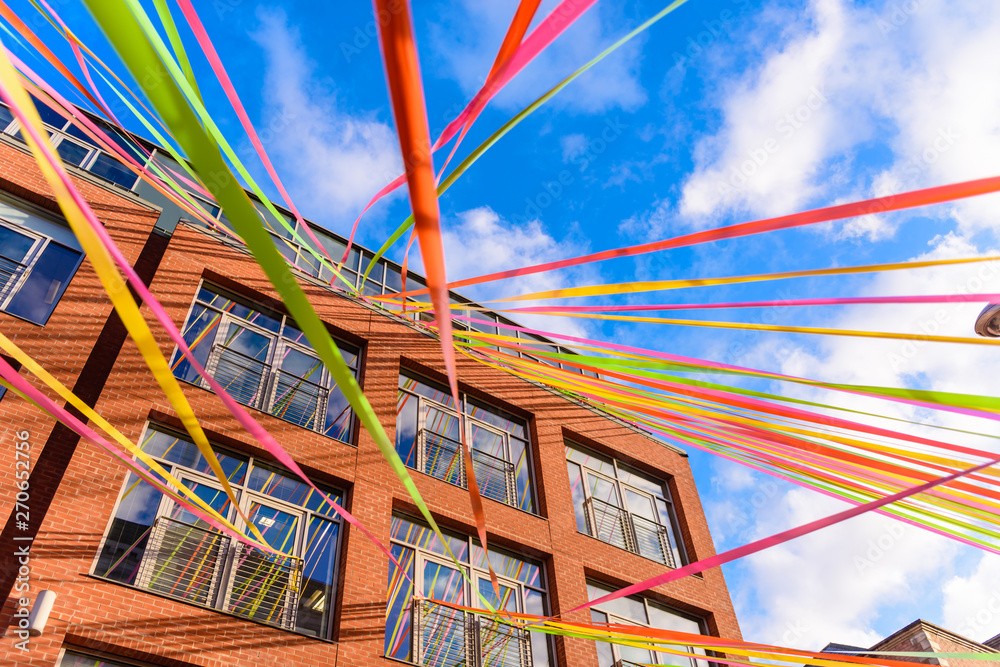 Multicoloured ribbons stream between buildings against a blue sky.