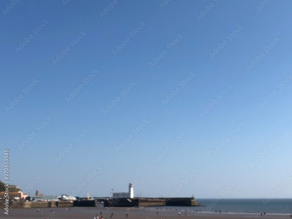Looking across beach at low tide towards the harbour lighthouse in Scarborough, UK on a bright blue sky sunny day