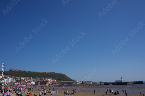 Looking across beach at low tide towards the harbour lighthouse in Scarborough, UK on a bright blue sky sunny day