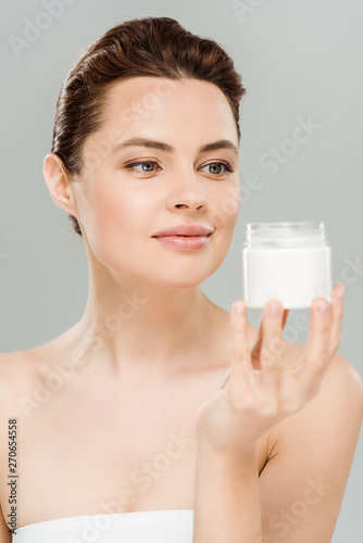 happy woman looking at container with cosmetic cream isolated on grey