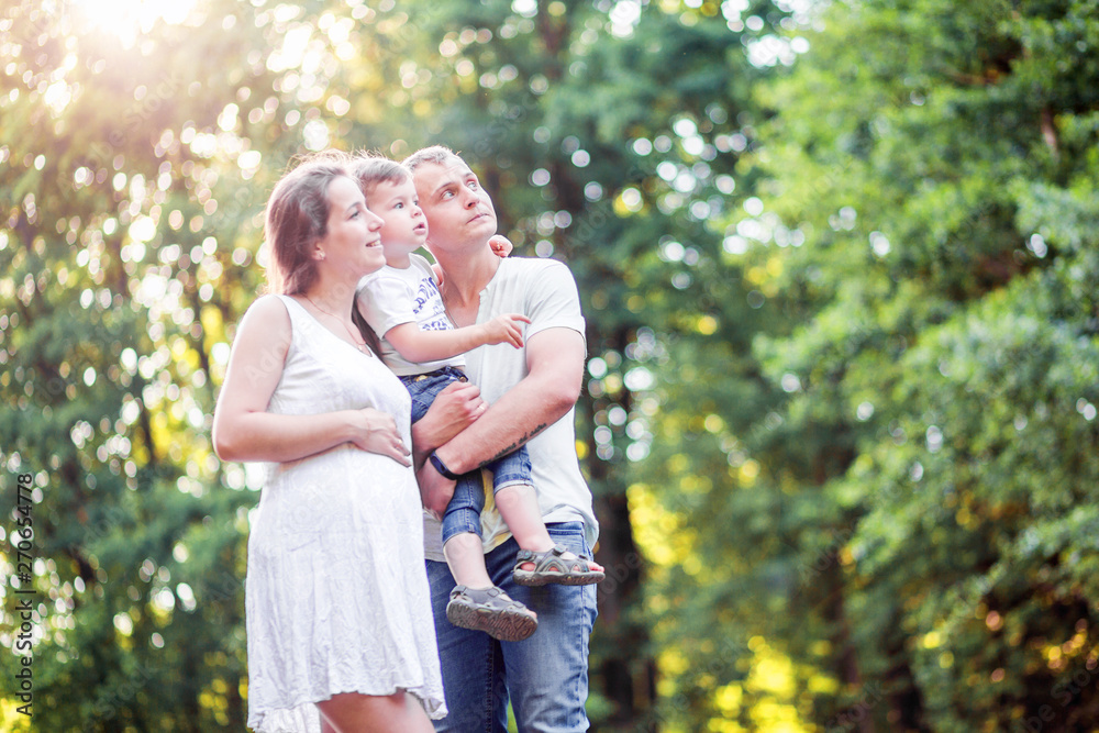 pregnant woman, her husband and son together for a walk in the park. Look somewhere up pregnant woman, her husband and son together for a walk in the park. Look somewhere up