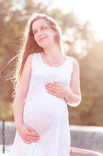 Pregnant woman near a pond in the rays of the evening sun