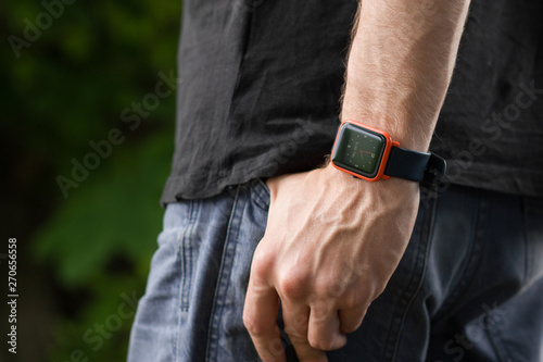 Smart watch close up photo. Man posing in summer park. Body detail on man’s hand in the jeans pants pocket.