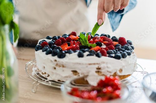 Young woman preparing a cream cake with fresh fruits photo