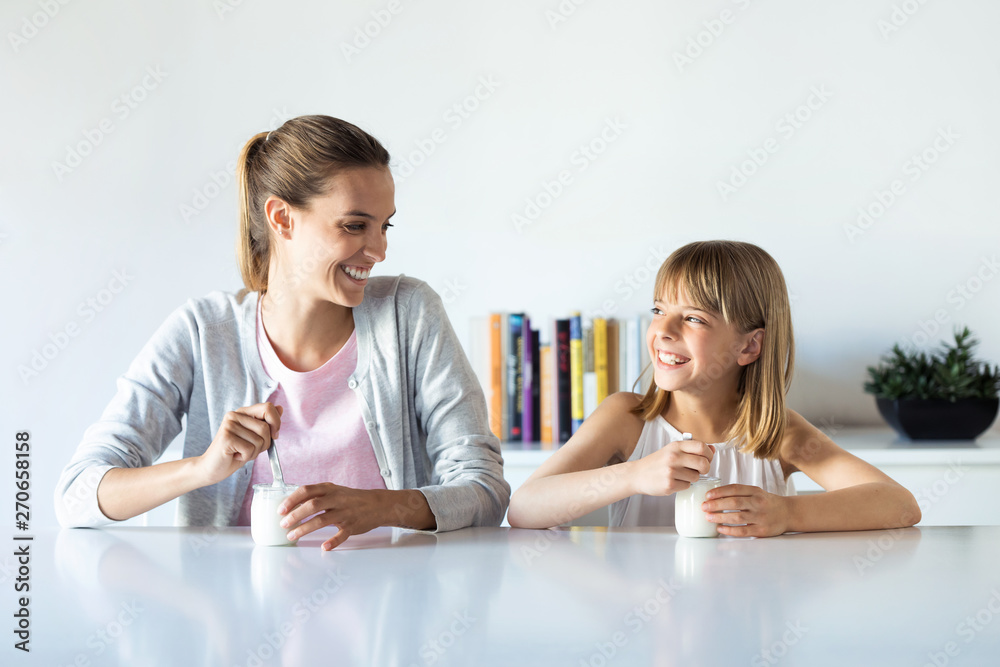 Pretty young mother and her daughter looking to each other while eating yogurt at home. Pretty young mother and her daughter looking to each other while eating yogurt at home.