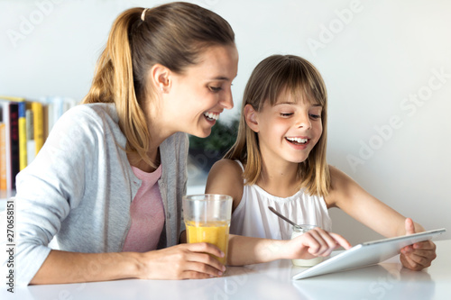 Pretty young mother and her daughter using digital tablet while having breakfast at home.