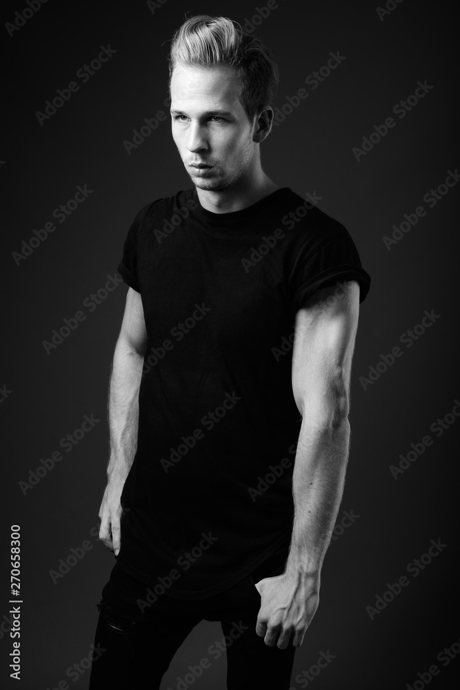 Studio shot of young handsome man against gray background in bla Studio shot of young handsome man against gray background in bla