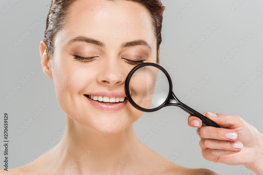 cheerful woman with closed eyes holding magnifying glass near face isolated on grey cheerful woman with closed eyes holding magnifying glass near face isolated on grey