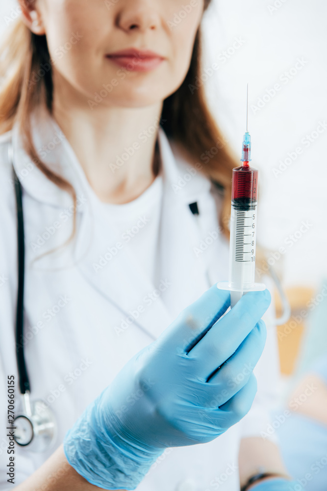 partial view of doctor in white coat holding syringe with blood sample partial view of doctor in white coat holding syringe with blood sample