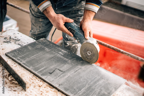 Construction site details - industrial tool, worker with angle grinder cutting marble and granite stone