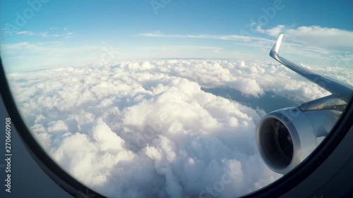Airplane flying slightly above the clouds. Inside view through the window of an airplane of the wing and turbine. Clouds moving fast below the plane. Brazilian terrain.