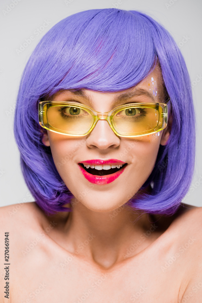 beautiful surprised girl in purple wig and sunglasses isolated on grey