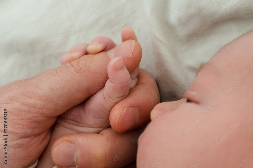 Hand of newborn baby holding male adults finger. Concept of help and family. Father holding hand.