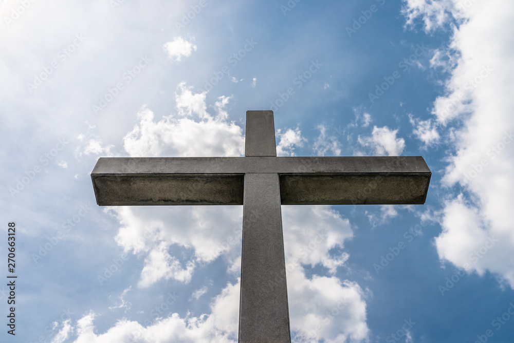 A large concrete cross on a cemetery against a blue sky with white clouds.