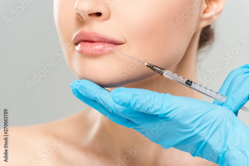 cropped view of cosmetologist in blue latex gloves holding syringe near face of woman isolated on grey