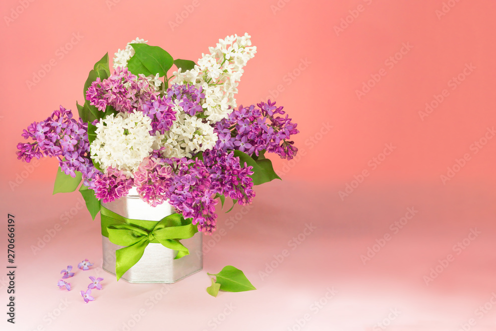 Bouquet white and purple lilac flowers in vase in a vase with a gift bow on table, copy space. PInk background.