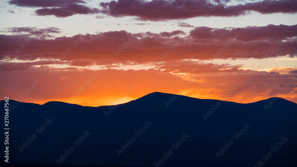 Obraz premium Zachód słońca tworzy pasmo górskie i barwi niebo i chmury na żółto, pomarańczowo, fioletowo i różowo - Góry Jemez w pobliżu Santa Fe w Nowym Meksyku
