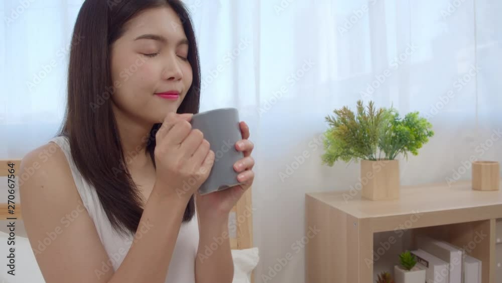 Happy beautiful Asian woman smiling and drinking a cup of coffee or tea on bed in the bedroom Lifestyle women at home concept. Slow motion shot. Happy beautiful Asian woman smiling and drinking a cup of coffee or tea on bed in the bedroom Lifestyle women at home concept. Slow motion shot.