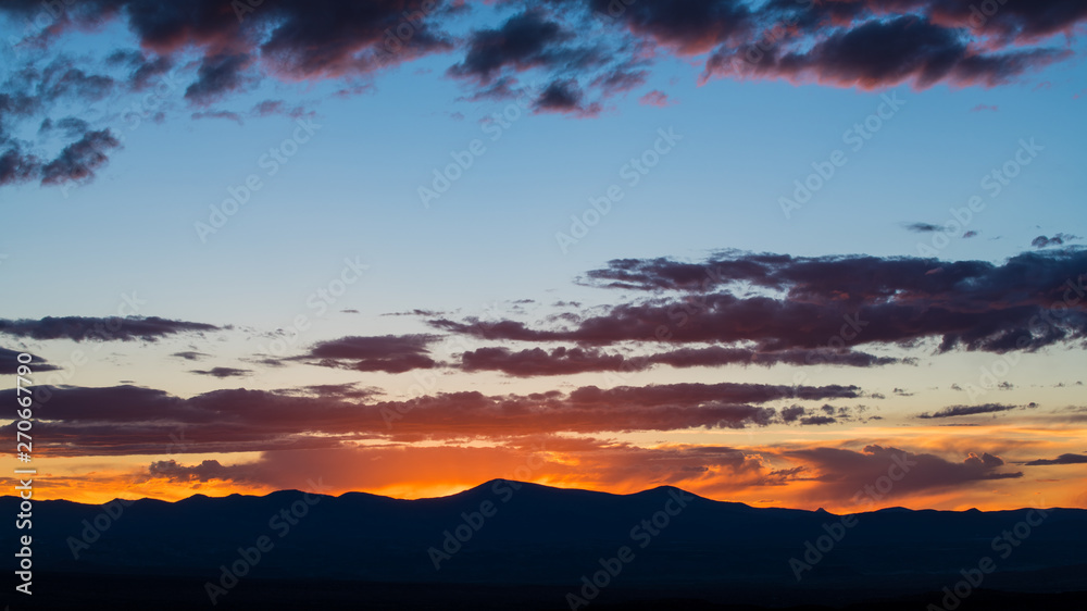 Naklejka premium Zachód słońca zarysowuje pasmo górskie i oświetla dramatyczne wieczorne niebo fioletowymi i różowymi chmurami - Góry Jemez w pobliżu Santa Fe w Nowym Meksyku